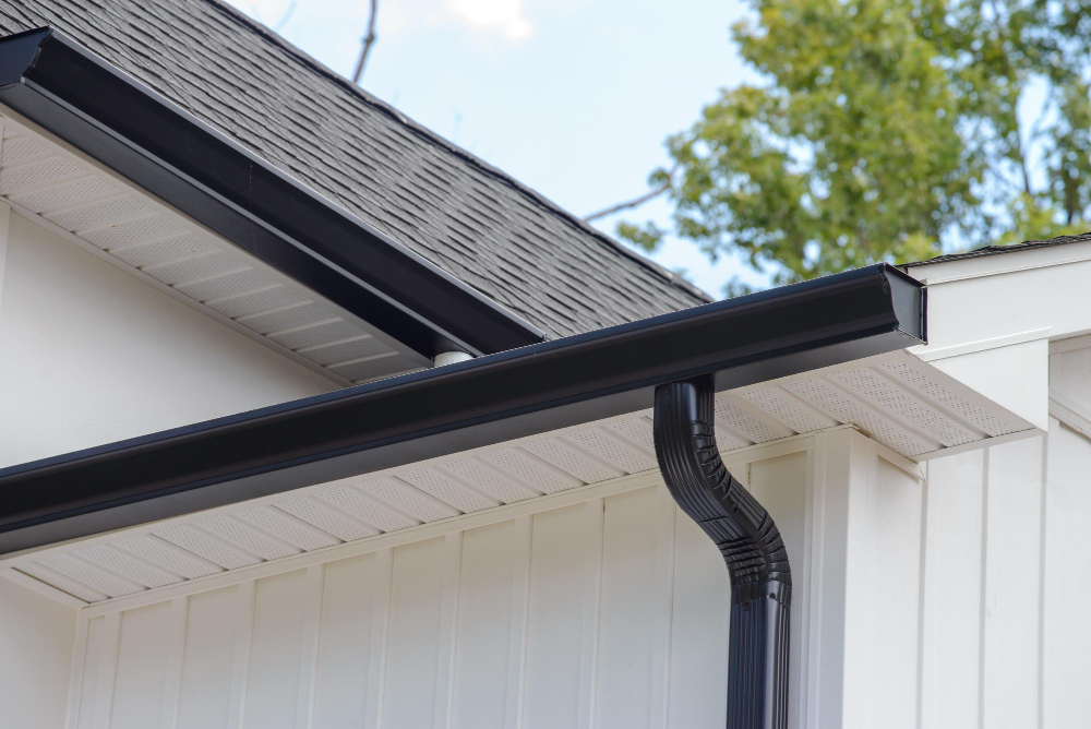 "Black aluminum rain gutter and downspout installed on modern white residential house"