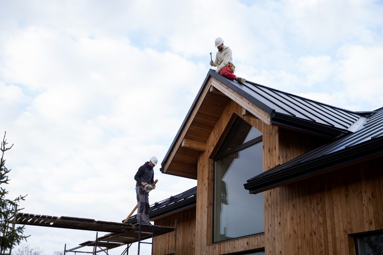 "Construction workers installing metal roofing on a modern wooden house"