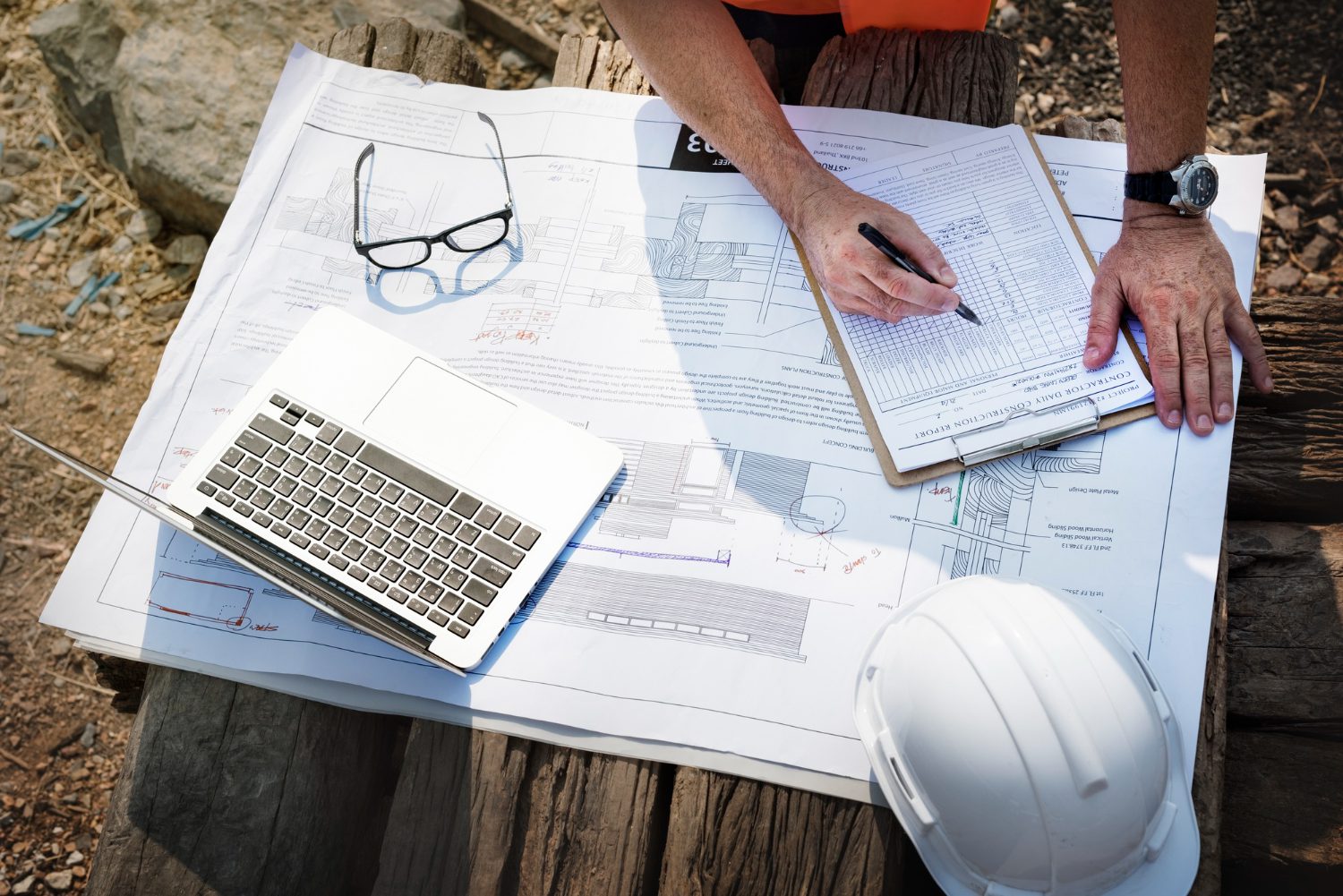 "Construction manager reviewing blueprints and checklist on site with laptop and safety gear"