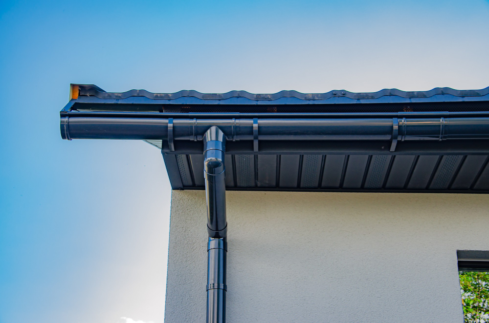 "Black metal rain gutter and downspout system installed on white residential building"