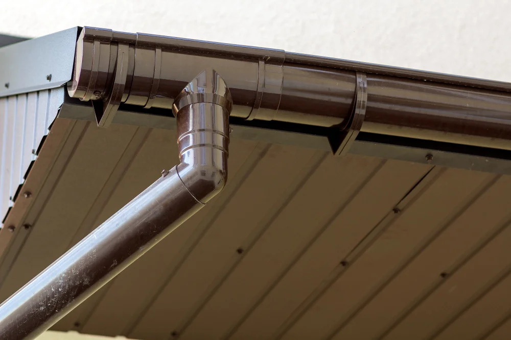 "Close-up view of dark brown metal rain gutter and downspout installed on house roof edge"