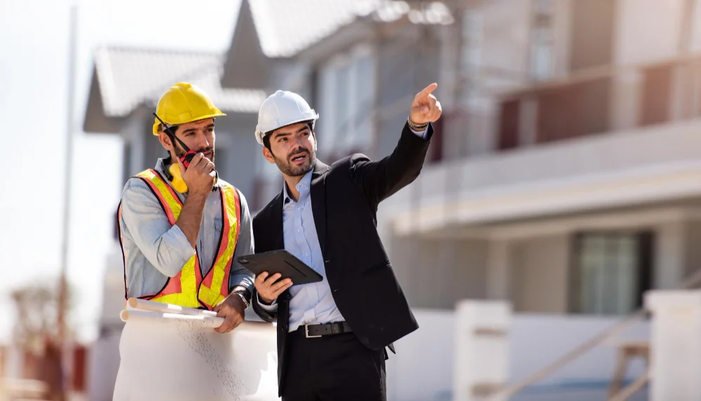 "Construction worker with walkie-talkie and site manager in suit discussing project at residential building site"