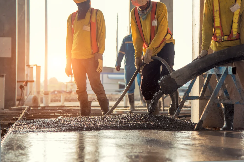 "Construction workers pouring and leveling concrete at a building site during sunset"