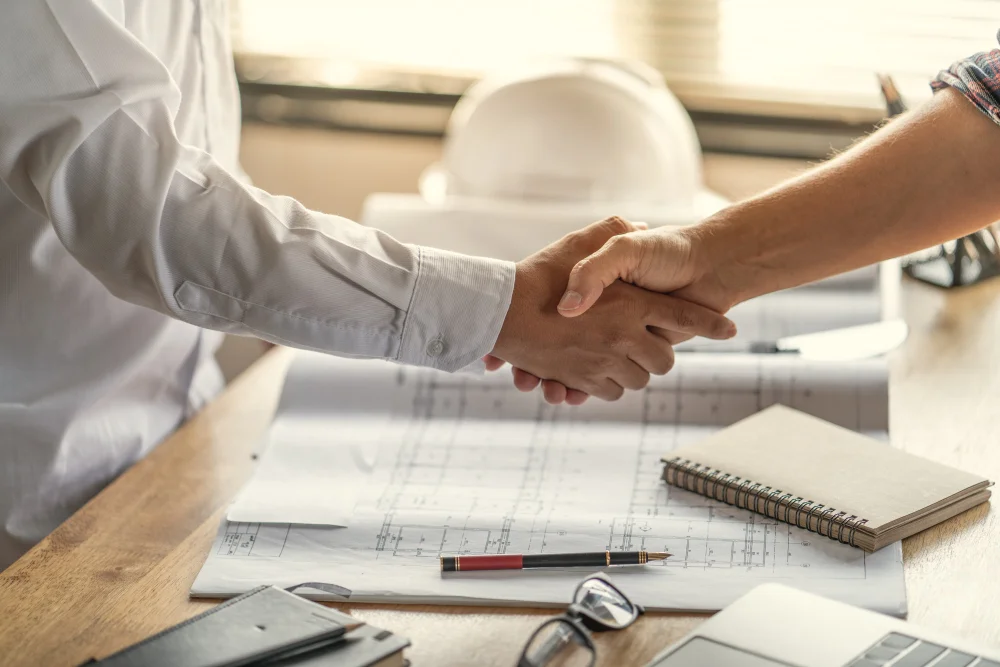 "Handshake between two professionals over construction blueprints and planning documents"