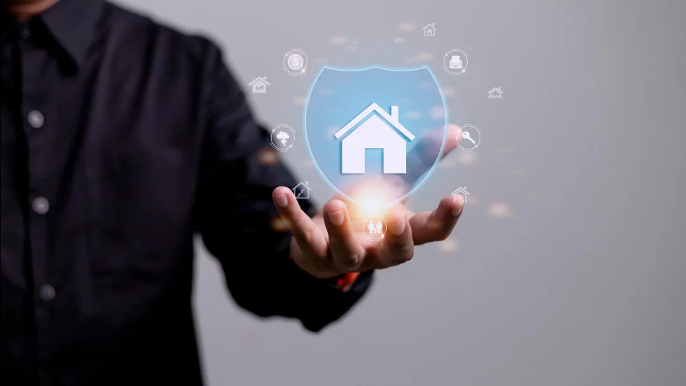 Person holding a digital shield with home icon and technology symbols, representing home security