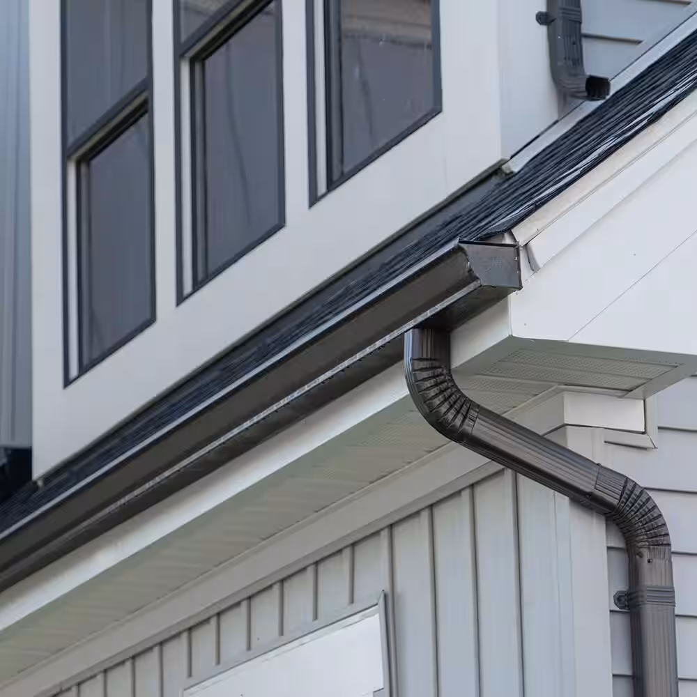 "Close-up view of a clean, modern black rain gutter and downspout attached to a white house exterior"