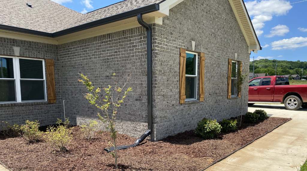 Downspout installed along brick wall directing water away from foundation