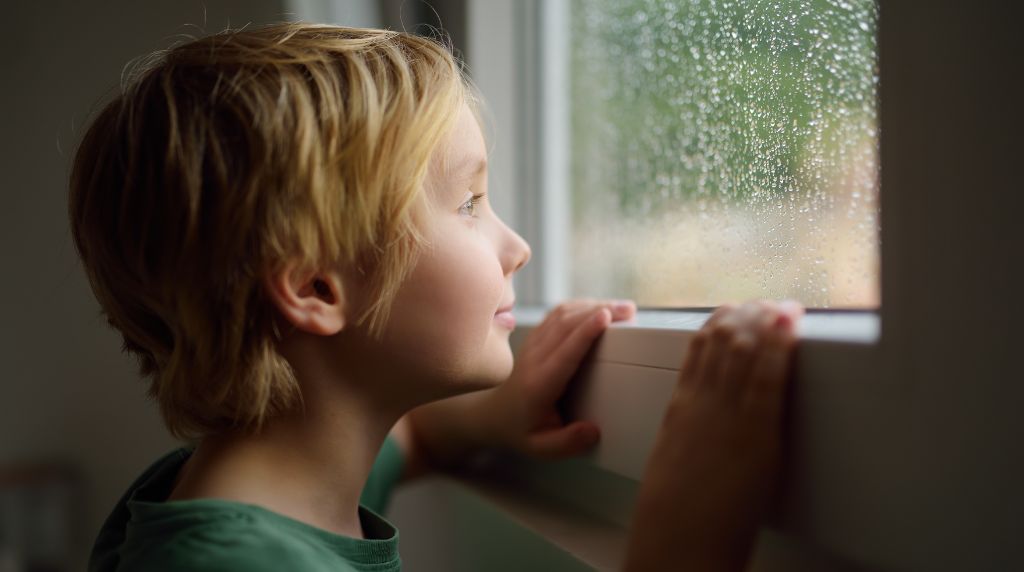 Child looking outside during rainy weather representing families missing outdoor living due to bugs and humidity in Tennessee