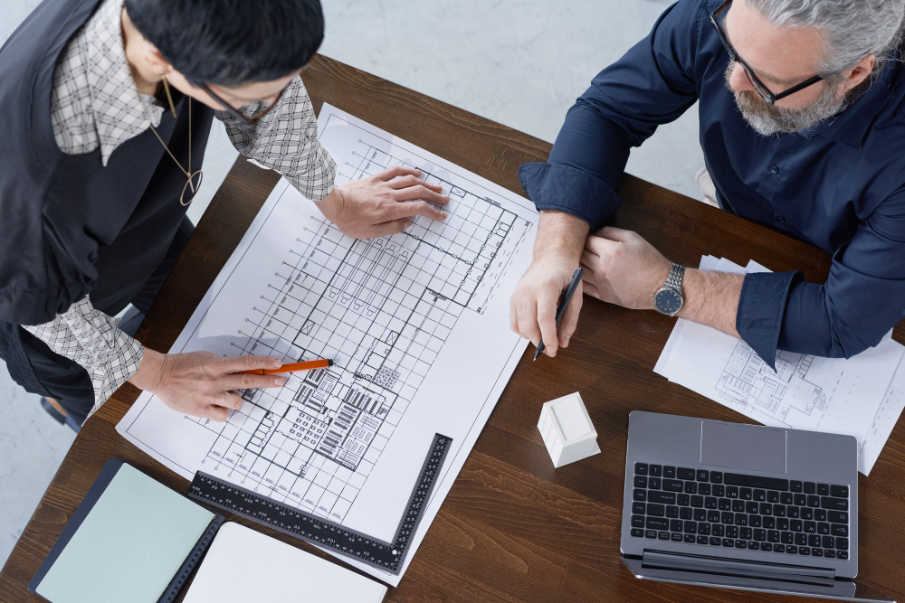 "Architects reviewing building blueprint and construction plans at a desk"