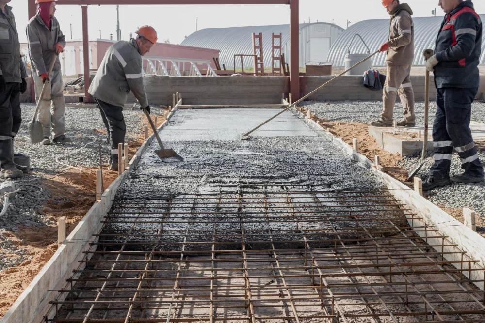 "Construction workers leveling freshly poured concrete over reinforced steel framework"