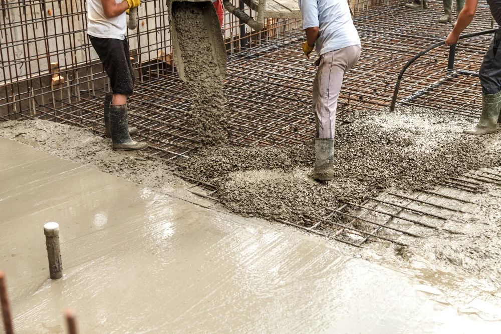 "Construction workers pouring and leveling concrete on reinforced steel foundation"