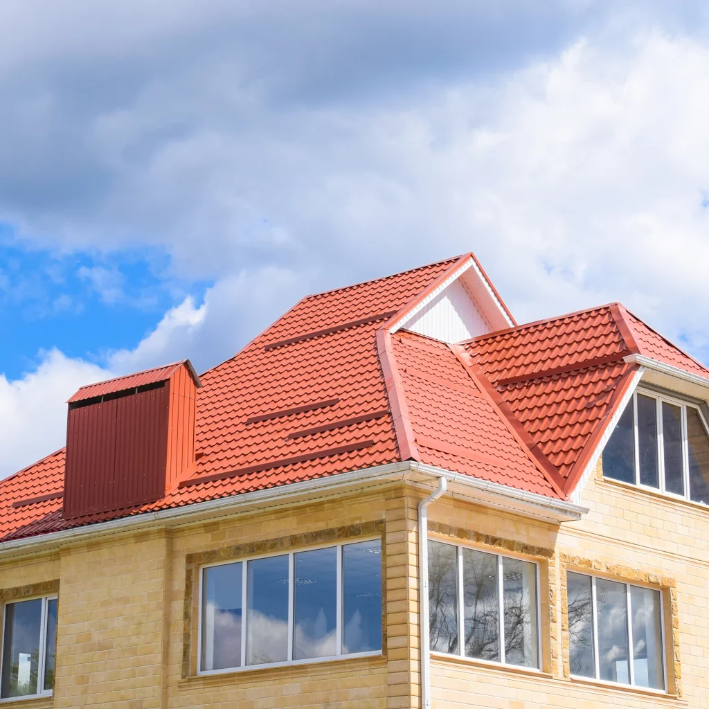 "Modern house with red tiled roof and large glass windows under a partly cloudy sky"